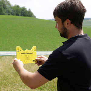 Mann bringt ein Warnschild am elektrischen Weidezaun an