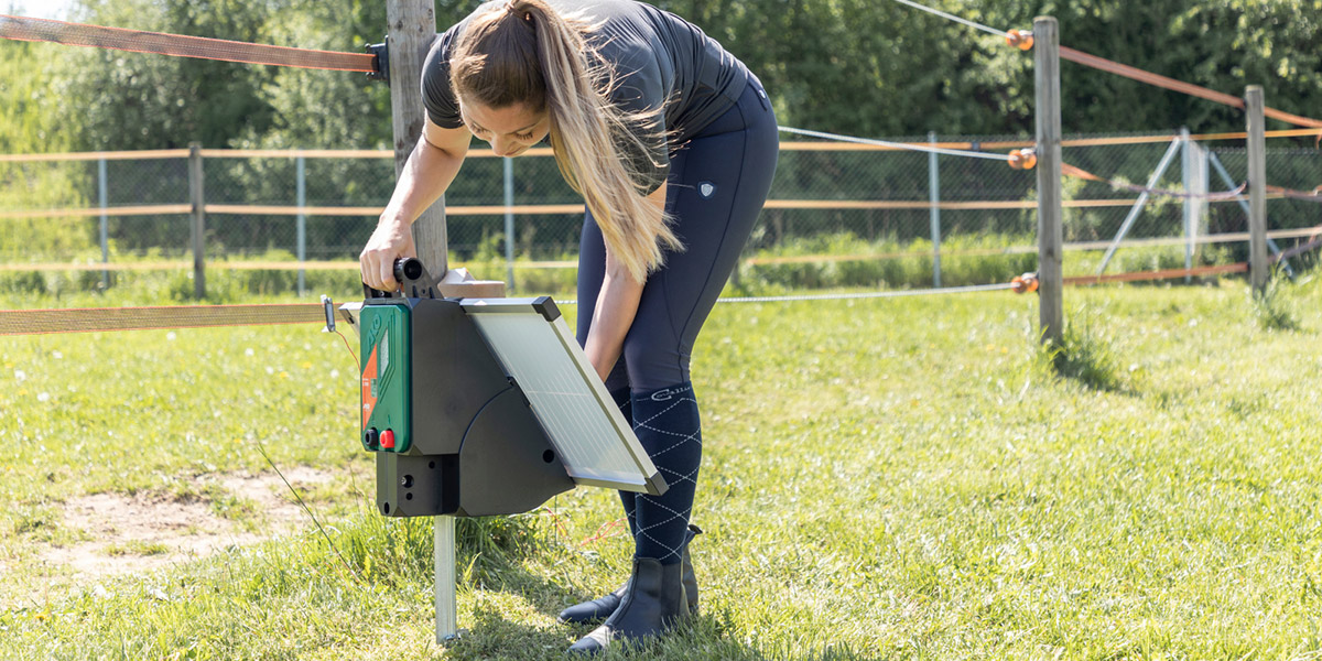 Landwirtin installiert ein Solar Weidezaungerät von AKO an einem elektrifizierten Weidezaun